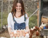 Uśmiechnięta kobieta w ogrodniczkach trzyma tacę z jajkami. To świetne sprzedaż bezpośrednia przykłady świeżych produktów prosto od kury.