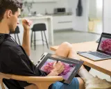 Un jeune homme utilise une tablette graphique pour créer une œuvre d'art numérique, sa configuration PC graphiste est prête pour l'inspiration.