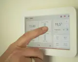 Un doigt interagit avec un écran tactile de domotique affichant la température et les programmes.