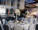 Elegancka sala weselna z białymi obrusami, kwiatami i oświetleniem tworząca magiczną atmosferę. To idealne miejsce na niezapomniane atrakcje na wesele.