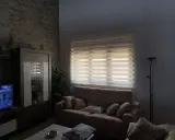 Salón acogedor con estores enrollables noche y día que filtran la luz, sofá, mueble y televisión.
