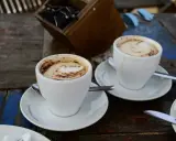 Zwei Tassen Kaffee Latte mit Milchschaum und Kakao-Muster auf einem Holztisch.