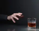 Mano tesa verso un bicchiere di whisky, un'immagine che evoca la domanda: quanto beve un alcolista al giorno?