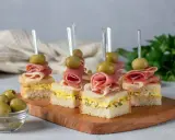 Eleganckie mini przekąski na imprezę: kanapki z szynką, jajkiem i oliwkami na wykałaczkach.