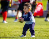 Niño feliz jugando con una pelota de fútbol americano, disfrutando de los juegos con pelotas para niños en un día soleado.