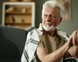 Anziano con bastone, forse per uno dei 10 sintomi parkinson. Sguardo pensieroso, coperto da una coperta a quadri.