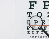Tablica optometryczna z lupą, która powiększa literę "P". Może to symbolizować problemy ze wzrokiem, jak astygmatyzm nabyty.