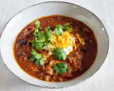 Gęste, aromatyczne chili con carne z fasolą, mięsem i przyprawami, udekorowane śmietaną, startym serem i świeżą kolendrą.