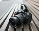 Czarny aparat Nikon D5600 z wysuniętą lampą błyskową leży na drewnianej ławce. Idealny do nikon d5600 test.