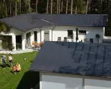 Familj njuter av solen på gräsmattan framför ett modernt hus med ett stilrent lindab solar roof.
