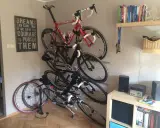 Jak zrobić wieszak na rower? Kilka rowerów wiszących na ścianie, obok półki z książkami i dekoracji.