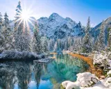 Morskie Oko zimą: ośnieżone drzewa odbijają się w turkusowej wodzie, a słońce przebija przez szczyty gór.