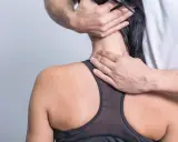 Hände massieren den Nacken einer Frau, die unter einem steifen Genick leidet.