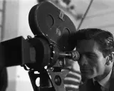 Pier Paolo Pasolini, con lo sguardo concentrato, osserva attraverso l'obiettivo di una cinepresa Arriflex, pronto a catturare la realtà.