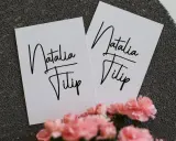 Dwie białe kartki z napisem "Natalia Filip" w ozdobnej czcionce. To piękne zasady zaproszenia na uroczystość.