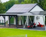 Maison moderne avec implantation panneau solaire sur le toit et le carport. Une tondeuse et un souffleuse à neige sont garés sous le carport.