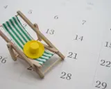Miniaturowa leżanka plażowa z zielono-białymi pasami i żółtym kapeluszem na tle kalendarza.