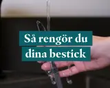 En hand håller ett bestick under rinnande vatten. Texten "Så rengör du dina bestick" visas.