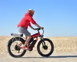 Mężczyzna w kasku i czerwonej bluzie jedzie na rowerze elektrycznym po piaszczystym terenie. Czy rower elektryczny ładuje się podczas jazdy?