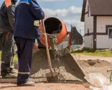 Robotnicy mieszają beton. Widać, ile piasku na worek cementu potrzeba do uzyskania odpowiedniej konsystencji.