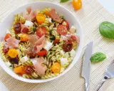 Une salade de pâtes originale avec des tomates cerises, du prosciutto, des dés de mozzarella et une sauce verte savoureuse.