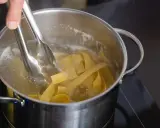 Szczypce do makaronu wkładają szerokie wstążki makaronu pełnoziarnistego do gotującej się wody w garnku.