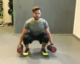 Mann macht Kniebeugen mit Kurzhanteln. Er hält zwei Hanteln mit je 14 kg Gewicht.