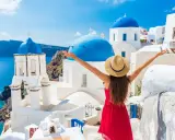 Kobieta w czerwonej sukience i kapeluszu cieszy się widokiem na Santorini. Idealne miejsce, gdzie do Grecji na wakacje!