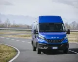 Niebieski Iveco Daily 3 na zakręcie drogi, z kierowcą za kierownicą. W tle góry i drzewa.
