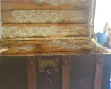 Baúl antiguo con chapa de latón oxidada y desgastada, listo para restaurar. El interior muestra restos de papel pintado.