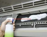 Mano rociando espuma para limpiar aire acondicionado unidad interior.