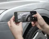 Ręce trzymają smartfon, fotografując reflektor i błotnik srebrnego auta. Sprawdzam lakierowanie elementu samochodu cennik.