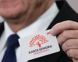 Dłoń trzyma białą kartę z czerwonym drzewem i napisem "KARTA SENIORA OGÓLNOPOLSKA".