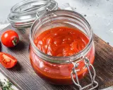 Domowy passata pomidorowa przepis. Słoik pełen gęstego sosu pomidorowego, obok świeże pomidory na desce.