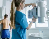 Technik przygotowuje aparat RTG do badania pacjenta. To właśnie RTG co to jest – badanie obrazowe wykorzystujące promieniowanie rentgenowskie.