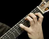 Main d'un guitariste jouant sur une microtonal guitar, ses doigts effleurant les cordes sur un manche sombre.