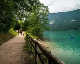 Passeggiata con il cane lungo il sentiero del lago di Santa Croce, con montagne verdi sullo sfondo e acque turchesi.