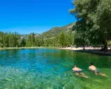Dos hombres nadan en la cristalina piscina natural Cañamares, rodeada de vegetación y montañas.