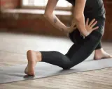 Kobieta ćwiczy jogę, pogłębiając skłon w wykroku, by rozciągnąć biodra i zniwelować tzw. hips dips.