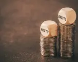 Dwie stosy monet, na jednej kostka z napisem "NETTO", na drugiej z napisem "BRUTTO".