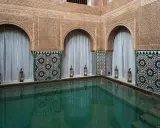 Ein ruhiger Pool im Hammam Al Andalus, umgeben von kunstvollen Fliesen und Schnitzereien, mit Kerzenlicht.