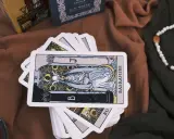 Karty tarota ułożone na brązowym materiale. Jedna karta, przedstawiająca postać z księżycem i owocami, jest na wierzchu. To idealny obrazek na **tarot na tydzień**.