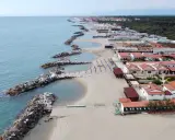 Vacker vy över pisa strand med sina stenpirar som bryter vågorna. Längre bort syns hus och en grönskande skog.