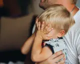 2,5-letnie dziecko budzi się w nocy z płaczem, ukrywając twarz w dłoniach. Tata tuli go, próbując uspokoić.