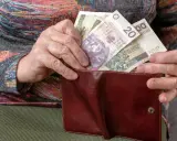 Dłoń starszej osoby wkłada polskie banknoty do brązowego portfela. Widać nominały 20, 100 i 50 złotych, stanowiące ekwiwalent codziennych wydatków.