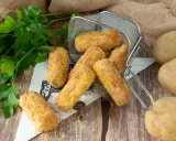 Crocchette di patate in friggitrice ad aria, dorate e croccanti, pronte per essere gustate. Accanto, patate fresche e prezzemolo.