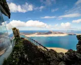 Blick vom Mirador del Río auf das Tal der tausend Palmen Lanzarote. Blaue See, Inseln und eine Hütte mit Glasfront.