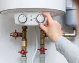 Main d'une personne ajustant le thermostat d'un chauffe-eau, contrôlant la pression de l'eau et la température.