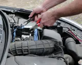 Ręce podłączają kable rozruchowe do akumulatora, próbując rozwiązać problem, dlaczego auto nie odpala.