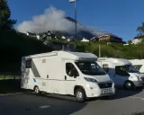 Husbil parkerad vid Trollstigen i Norge. Husen klättrar uppför den gröna sluttningen mot molnen.